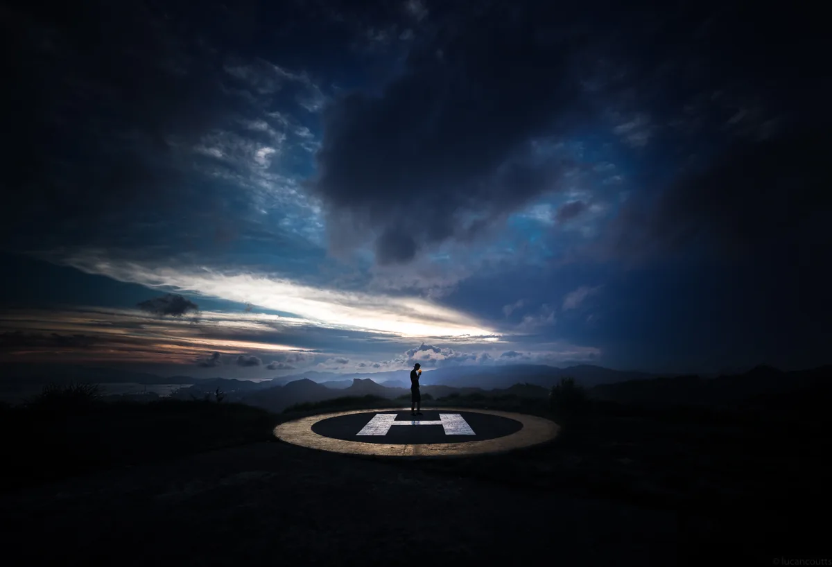 A lone figure on a helipad under dramatic night clouds in Hong Kong