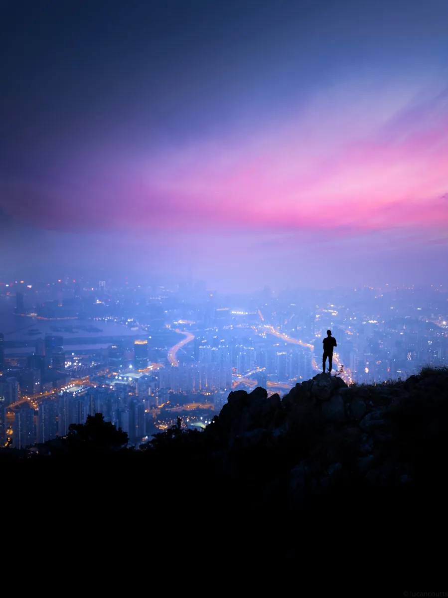 A figure on a hilltop overlooking Hong Kong in purple dusk haze