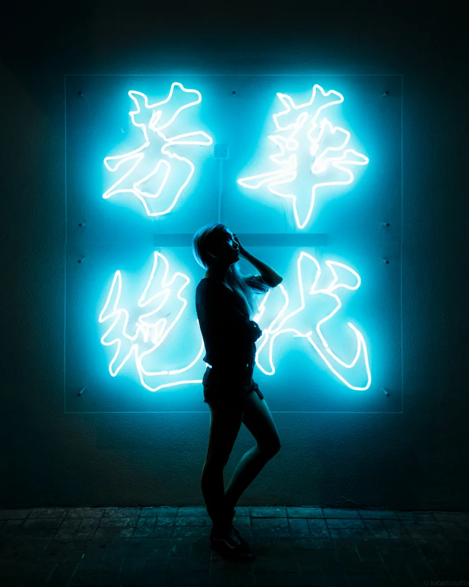 A silhouetted figure in front of a glowing blue neon sign with Chinese characters in Hong Kong