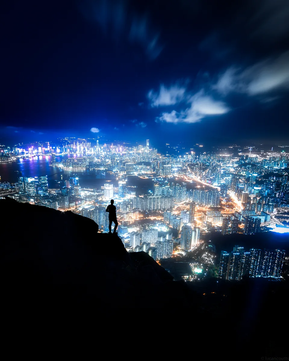 A figure on a rocky lookout above the lights of Hong Kong at night