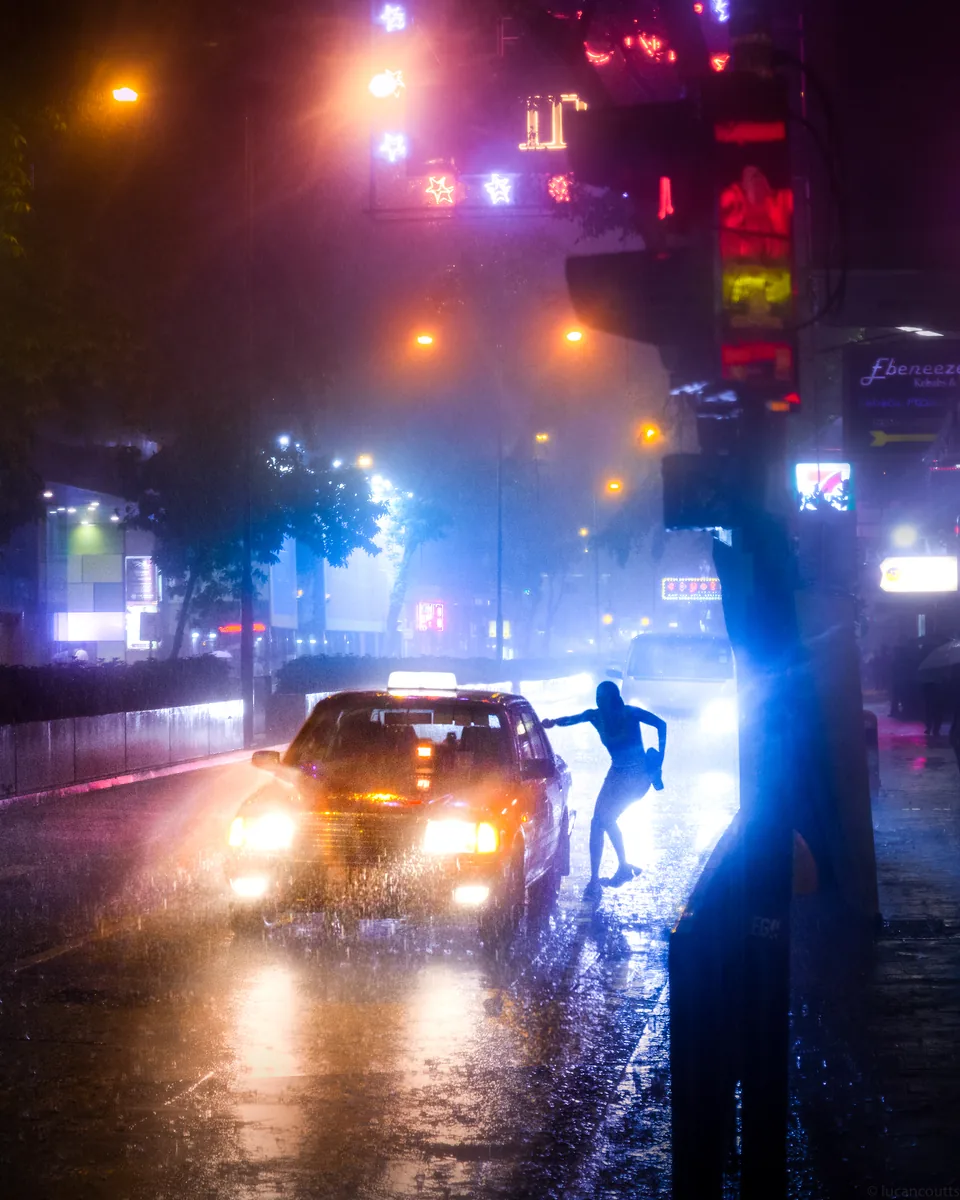 Don't Go, car headlights and neon light on a Hong Kong street at night with a figure in the glare