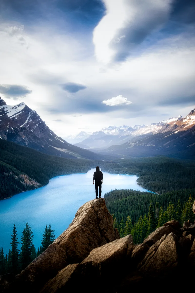 A figure standing on a rocky outcrop above the turquoise water of Peyto Lake in Banff National Park