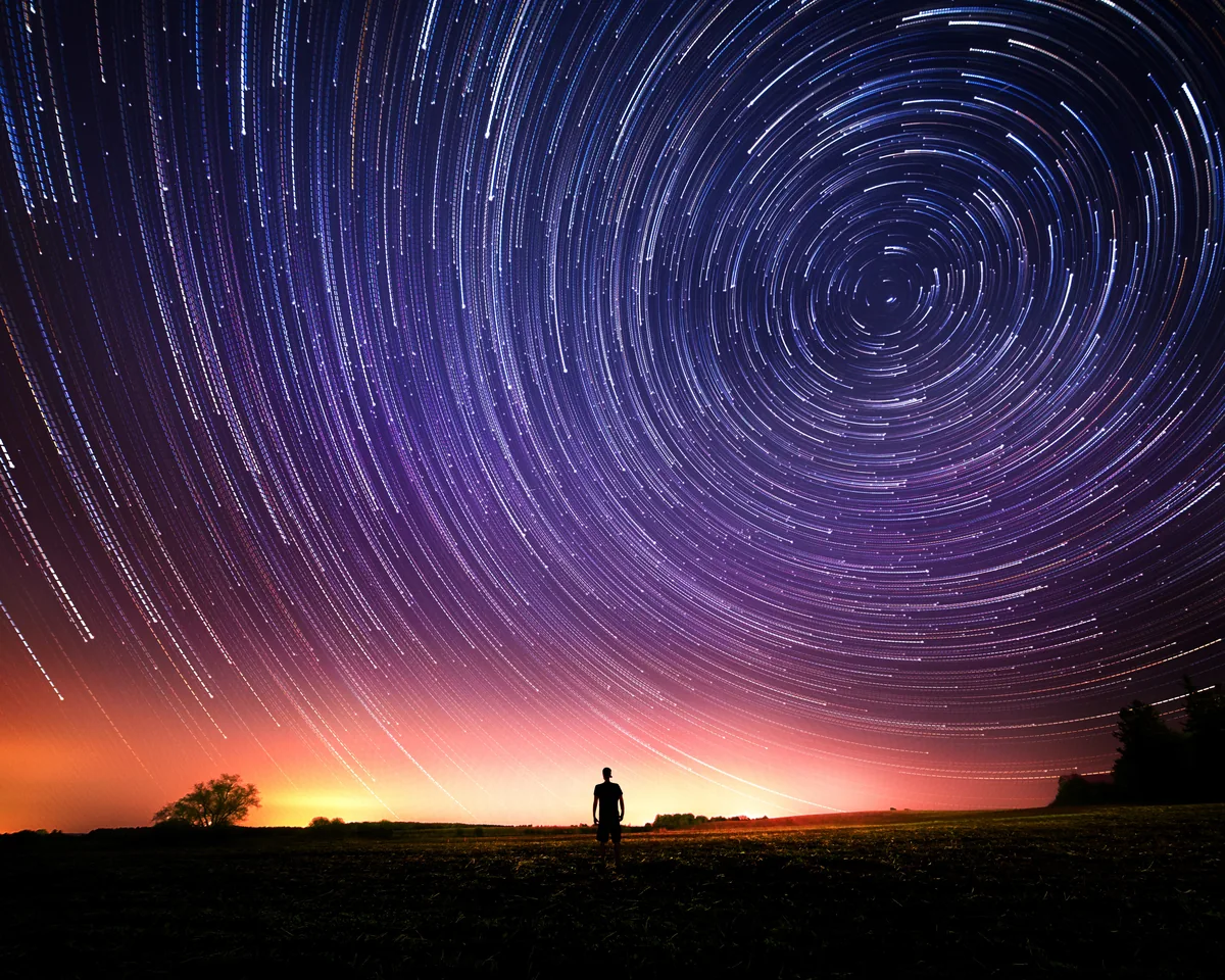 Circular star trails over a figure on the horizon near Scugog, Ontario, with a warm glow below