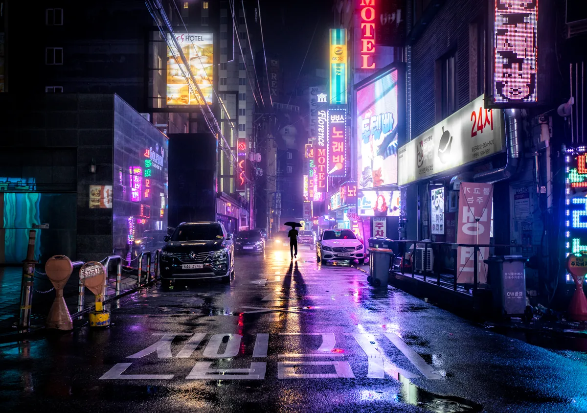 A Seoul street at night glowing with pink and purple neon reflected on wet pavement
