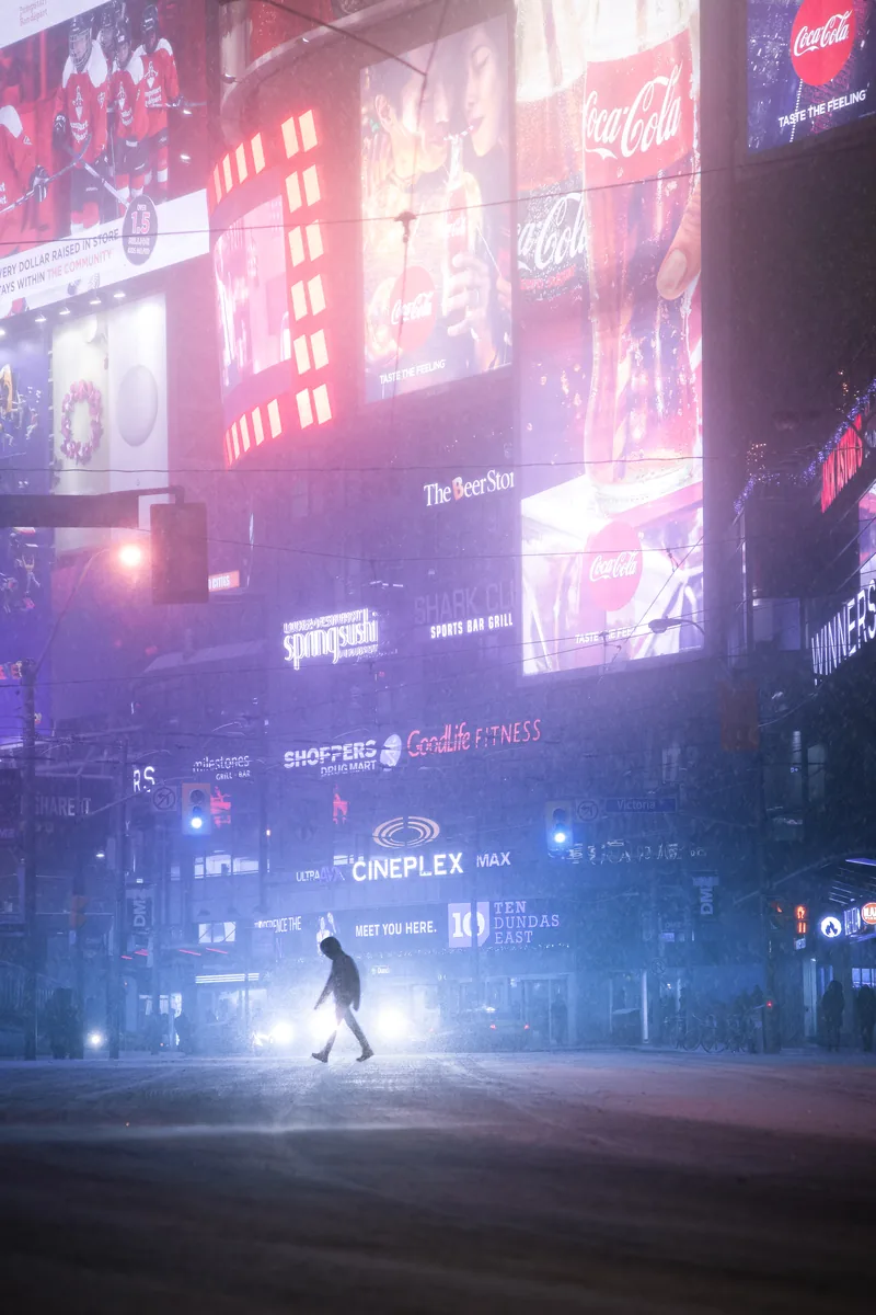 2049, a lone figure crossing a neon-lit street beneath towering screens and signs, a vision of Toronto in 2049