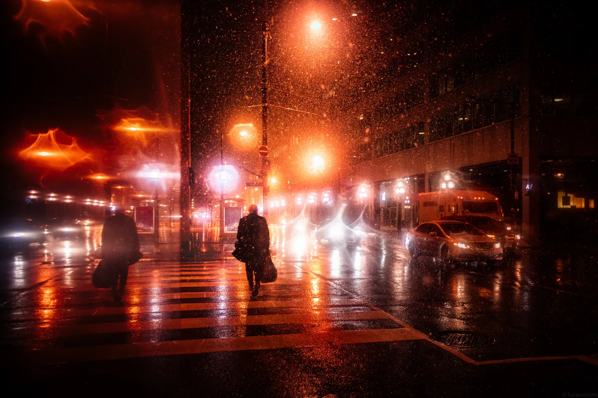 Static, pedestrians crossing through a snowstorm under orange streetlights in Toronto's Financial District