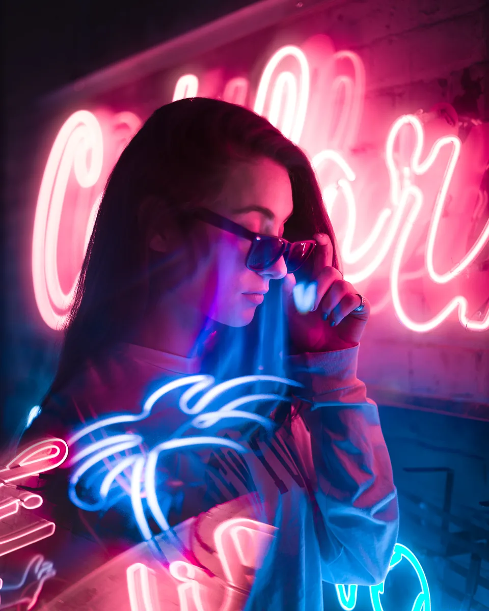 A portrait of a woman in sunglasses lit by pink and blue neon in Toronto